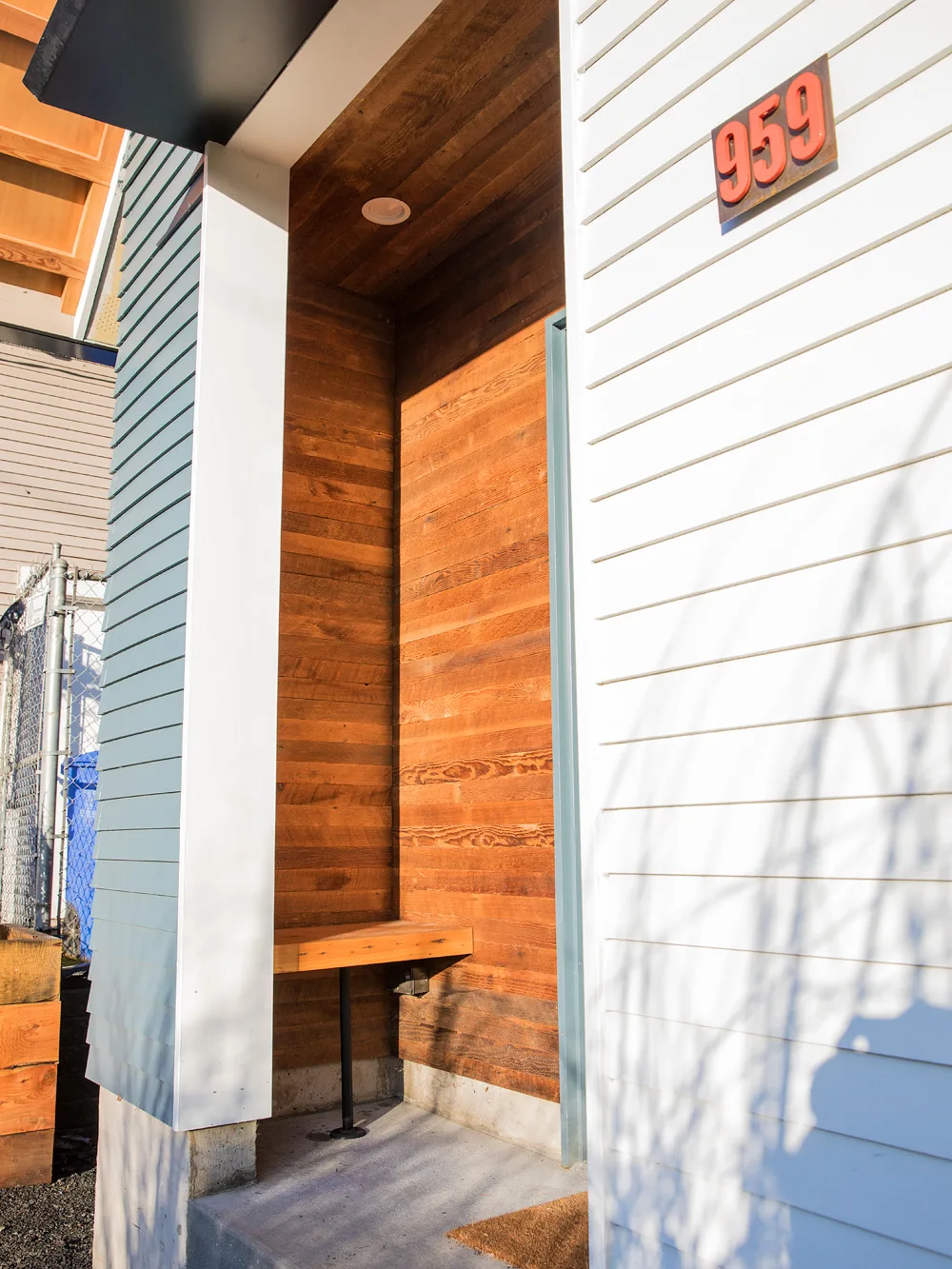 Entry porch of Mason Street ADU with cedar wood siding, a small built-in bench, and recessed lighting.