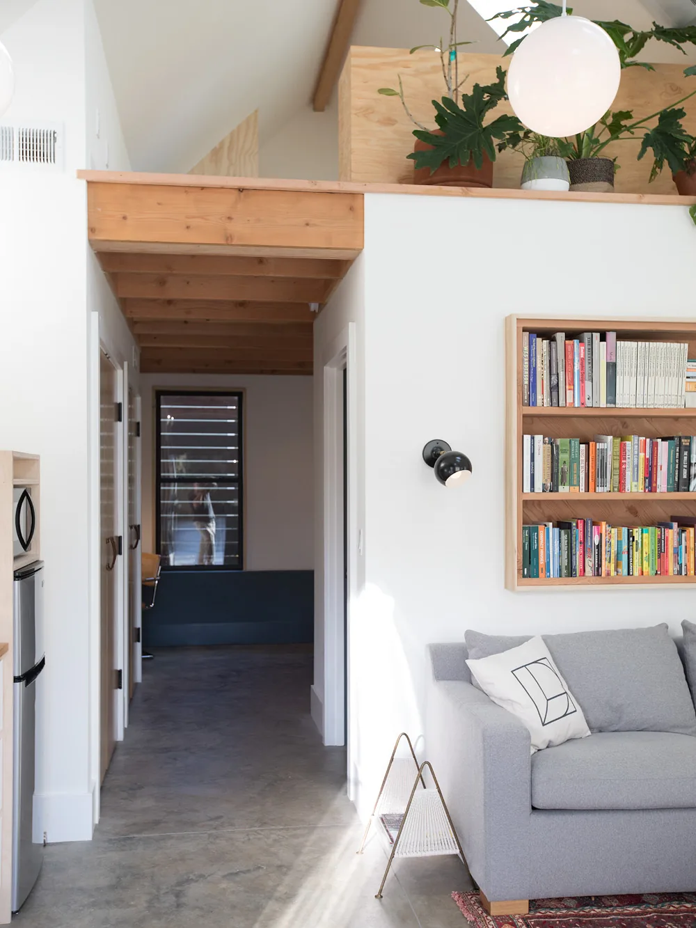 Hallway with exposed wood ceiling beams, concrete floor, a gray sofa, and a built-in bookshelf in the Mason Street ADU.