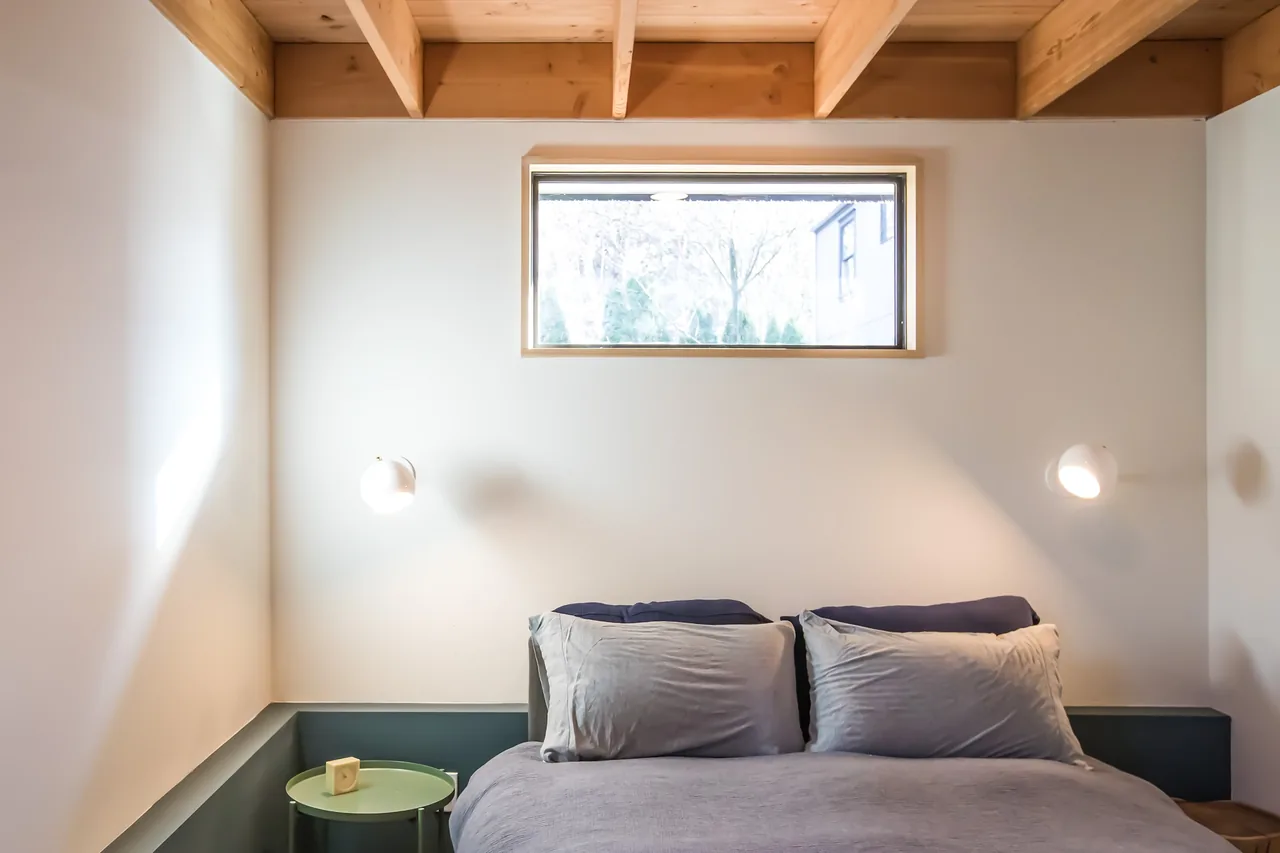 Bedroom in Mason Street ADU features exposed wooden ceiling beams and a horizontal window above the bed.