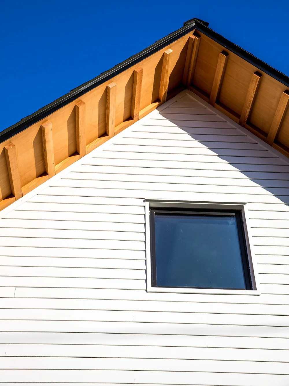 The Mason Street ADU features white wood siding with exposed wooden rafters and a square black-framed window.