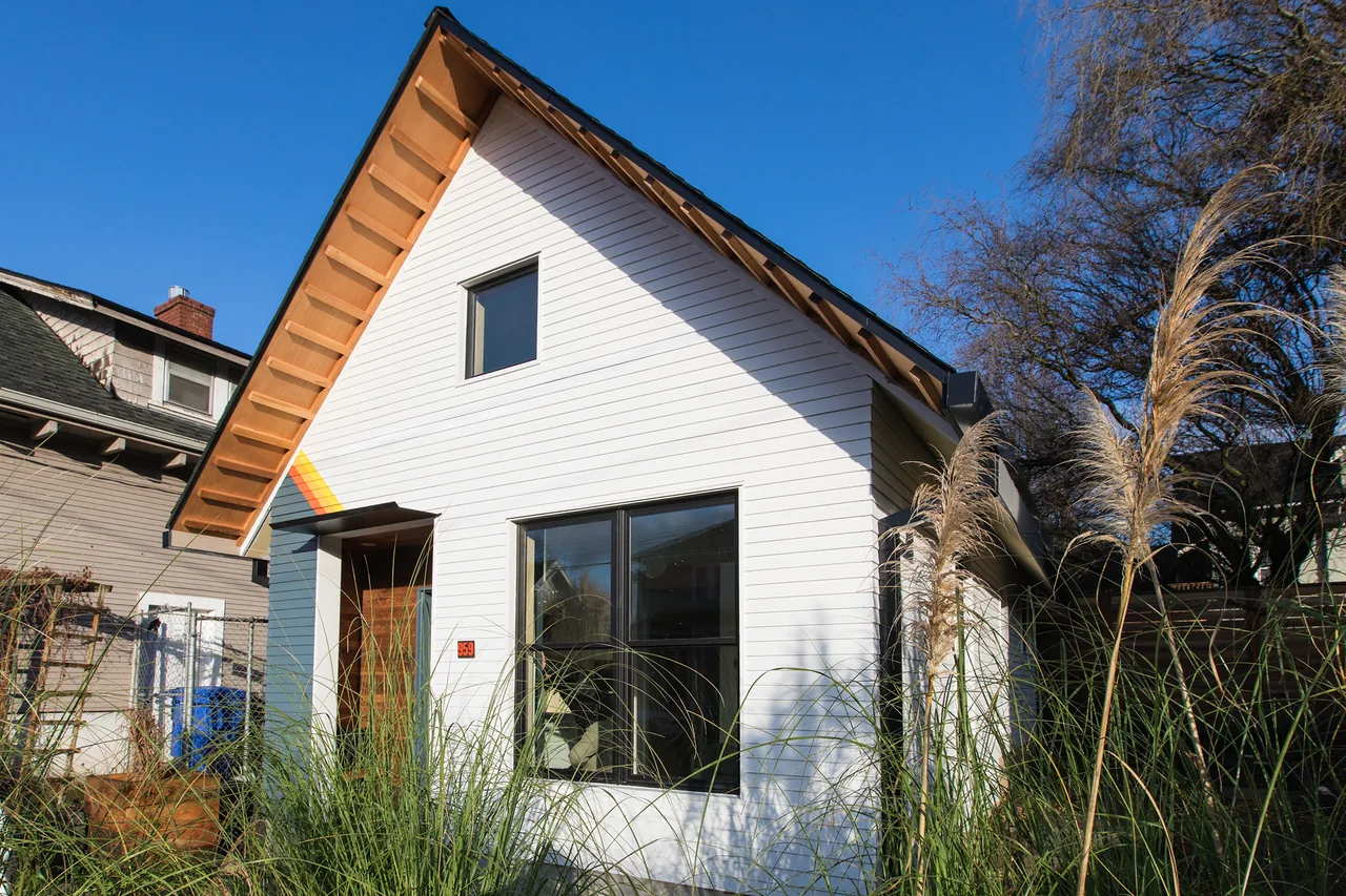 Mason Street ADU features white wood siding, black window frames, and a natural wood door under a steep gable roof.