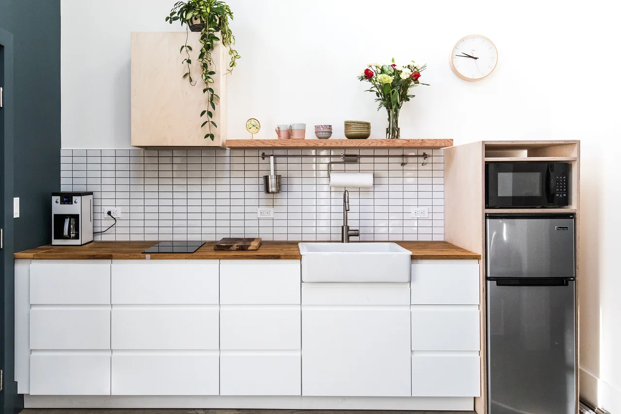 Small kitchen featuring white cabinetry, wooden counters, farmhouse sink, and built-in microwave and refrigerator.