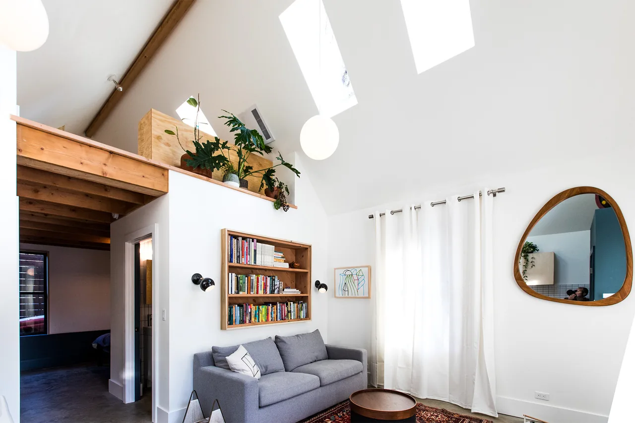 Living room with vaulted ceiling, exposed wooden beams, skylights, built-in bookshelf, and gray sofa in Mason Street ADU.
