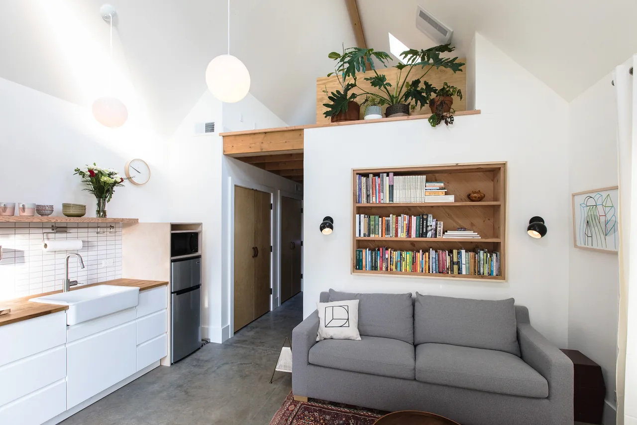 Mason Street ADU living room with exposed rafters, built-in bookshelf, and white kitchen cabinetry.