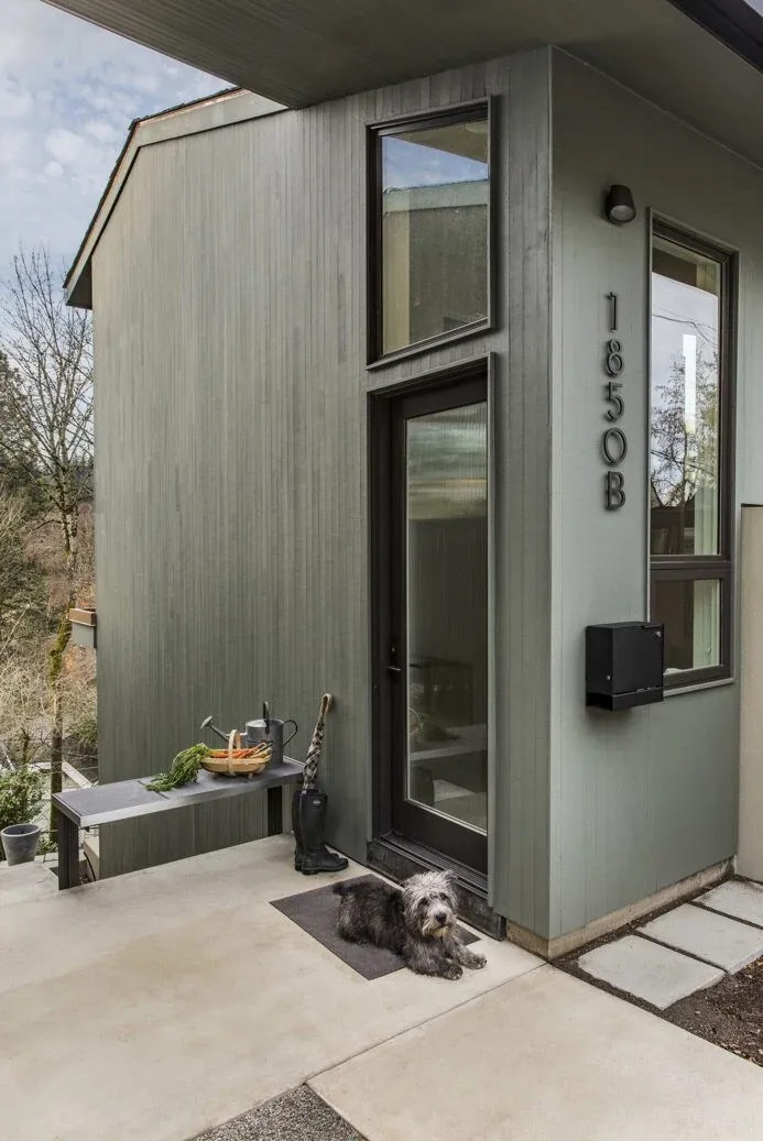 Gray vertical wood siding exterior with black framed glass door and windows showing mid-century inspired ADU design.
