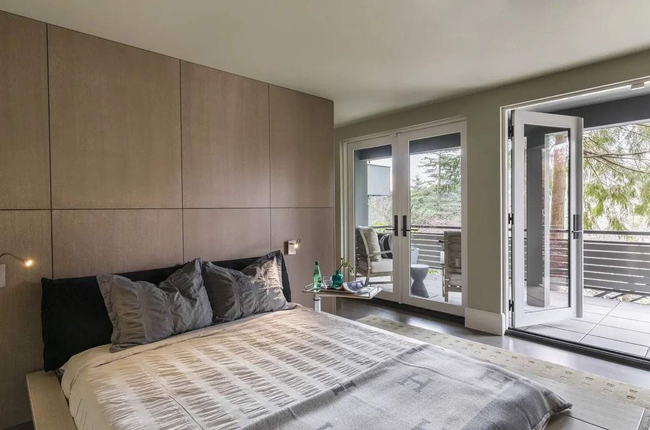 Mid-century inspired bedroom features wood panel wall and glass doors opening to a balcony with seating.