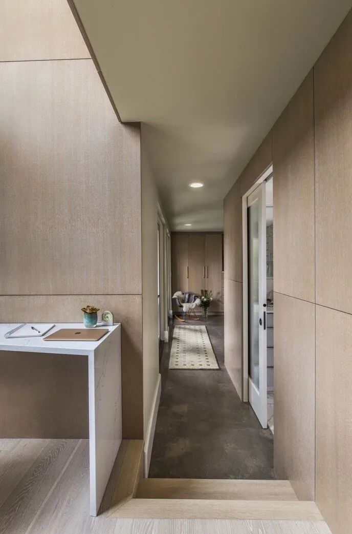 A narrow hallway with polished concrete flooring leads to a sitting area with built-in storage in the Mid-century Inspired ADU project.