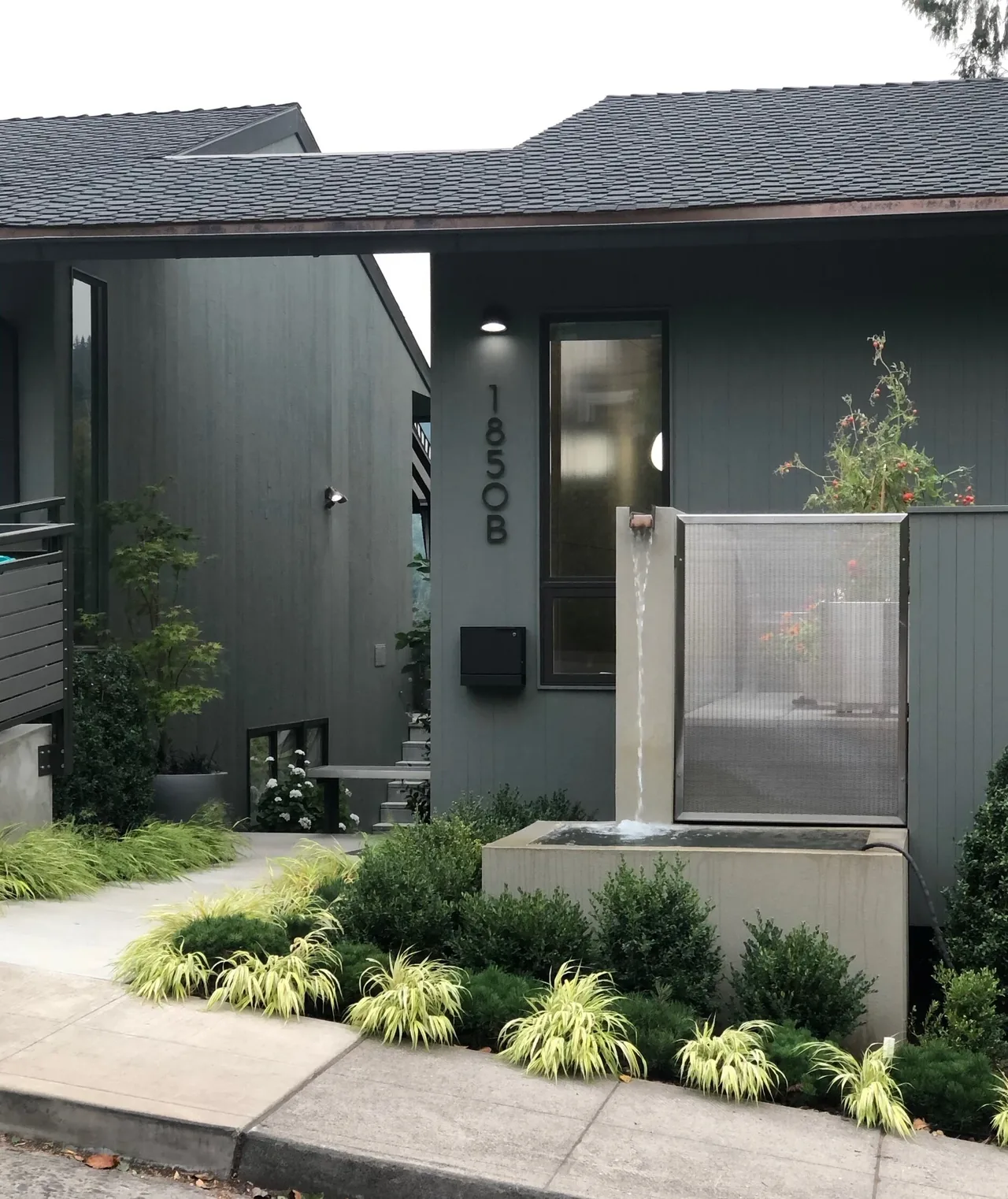 Mid-century inspired ADU exterior with gray wood siding, sloped roof, and water fountain at entrance.