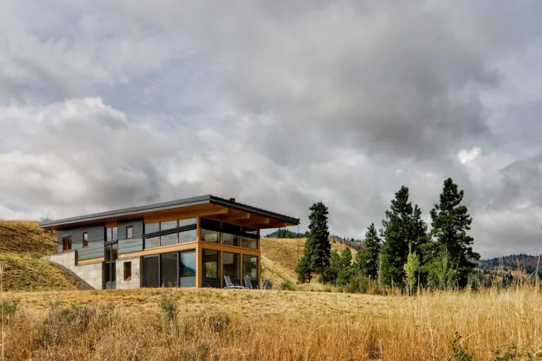 The Nahahum Canyon Residence features corner windows and an overhanging roof, set on a hilltop with natural surroundings.