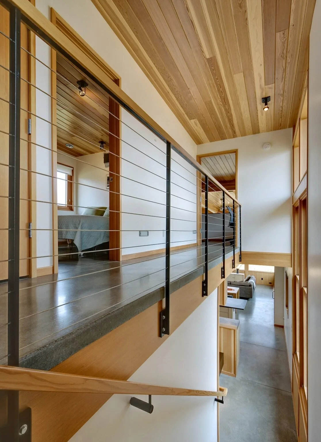 View along an interior hallway with cable railing, wood ceiling, and polished concrete flooring looking toward living space below.