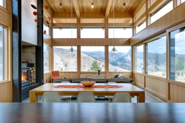 Living and dining area with floor-to-ceiling wood windows showcasing a hillside view in the Nahahum Canyon Residence by Studio Zerbey.