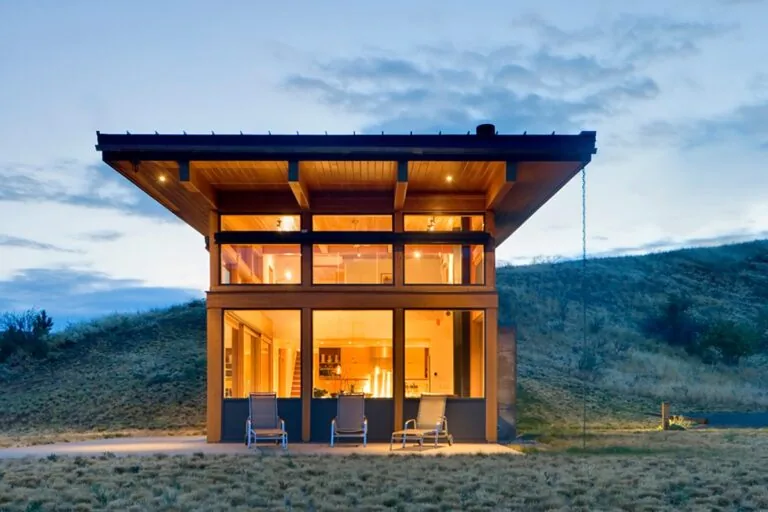 Nahahum Canyon Residence shows expansive wood window frames under a flat roof with wood ceiling beams visible inside.