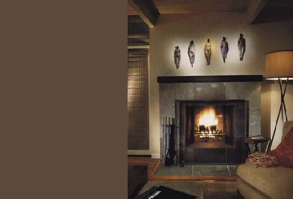 Living room fireplace with stone surround and wooden ceiling beams, featuring abstract sculptures on the wall.