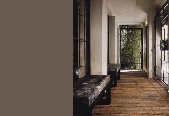 This narrow hallway features rustic wooden floors, black benches, and metal-barred windows and doors with natural light from outside.