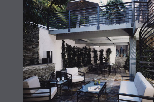 This outdoor patio features upholstered seating, a barred metal railing balcony, textured stone flooring, and stone wall accents.
