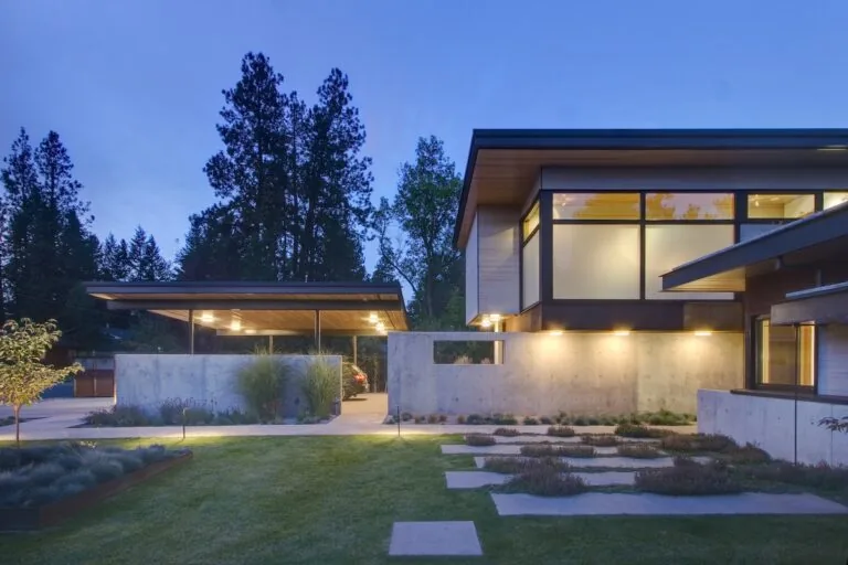 Montana Creekside Residence features concrete walls, large windows, and flat roofs with exterior lighting at dusk.