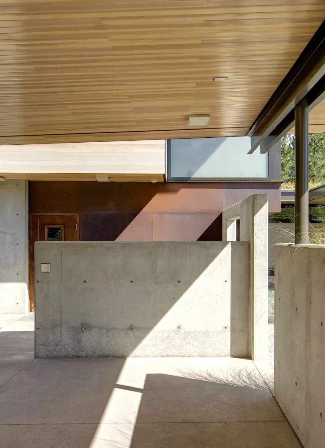 Covered exterior entry with concrete walls, wood-paneled ceiling, and frosted window creating a transition space.