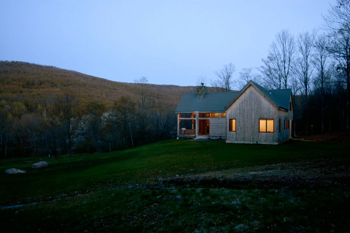 The Catskills Retreat by Stanev Potts Architects features a wood exterior with a covered porch overlooking a hill and forest.