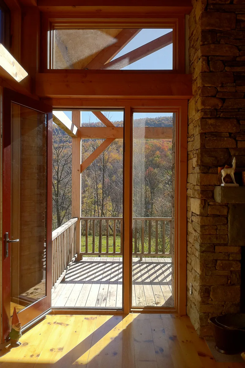 Interior view showing door opening to an open timber porch overlooking a wooded hillside in fall colors.
