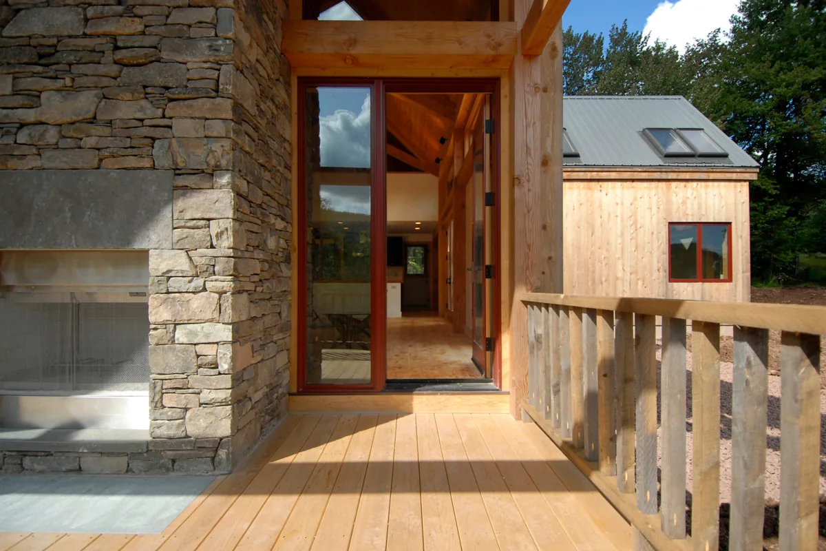 Porch with stone fireplace and wood railing at Catskills Retreat by Stanev Potts Architects.