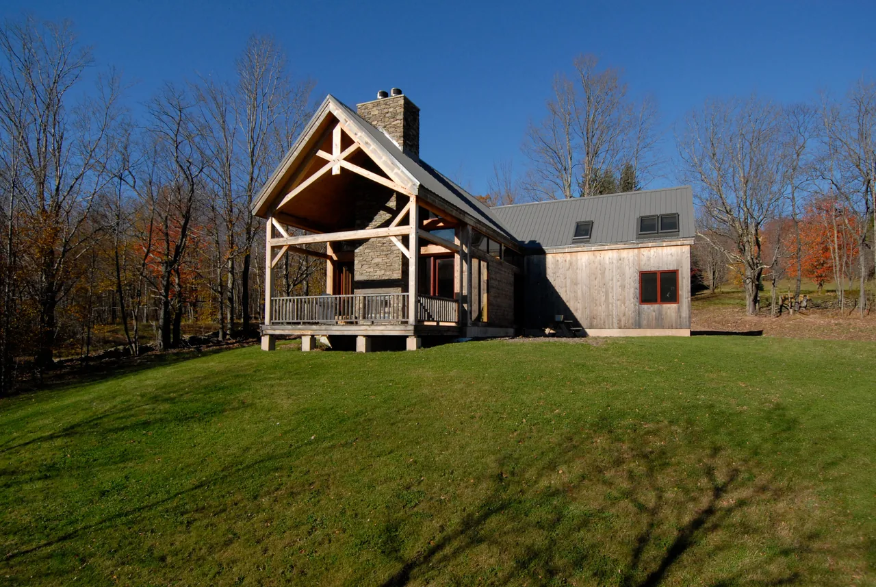 Catskills Retreat features a wooden cabin with a open porch, stone chimney, and a metal gable roof.