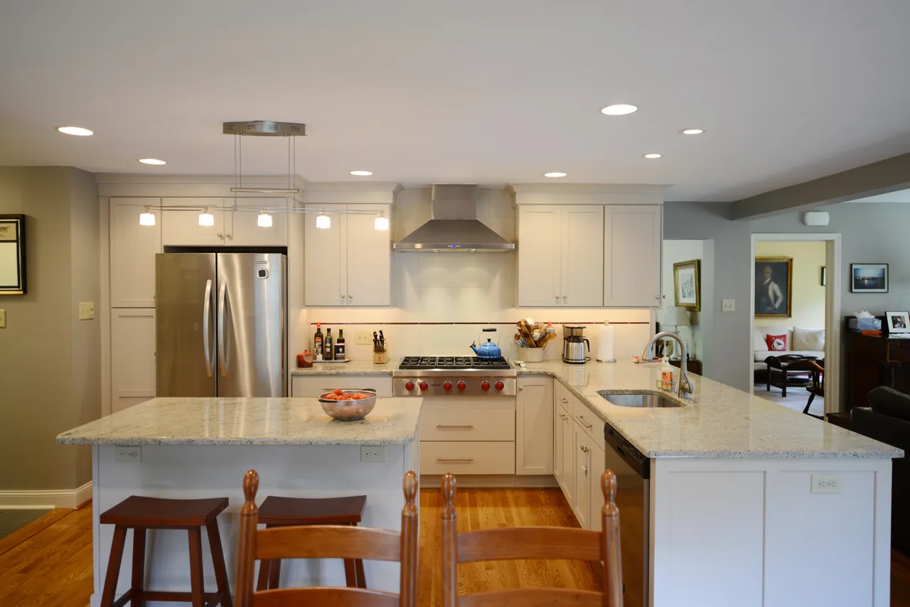 The Church residence kitchen features white cabinets, stainless steel refrigerator and range, and a spacious granite island with wooden stools.