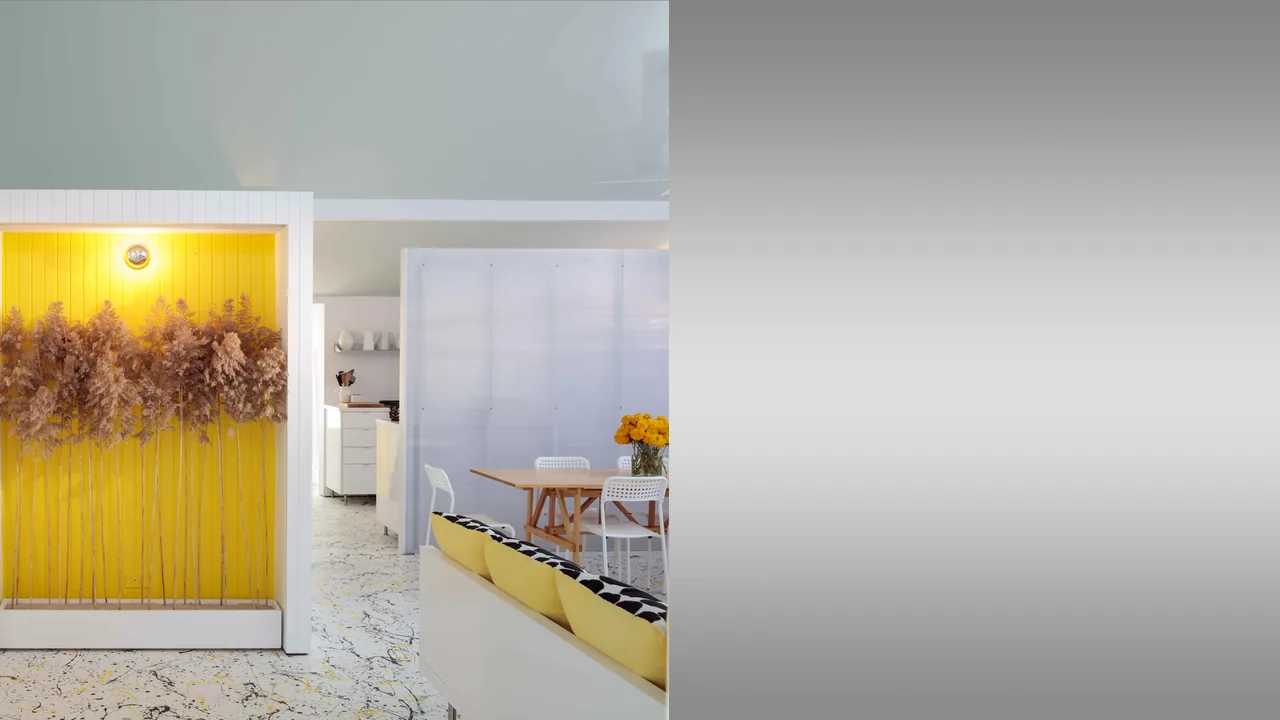 The Spagnola House features a yellow accent niche with dried floral arrangement beside the dining area with white chairs and wooden table.