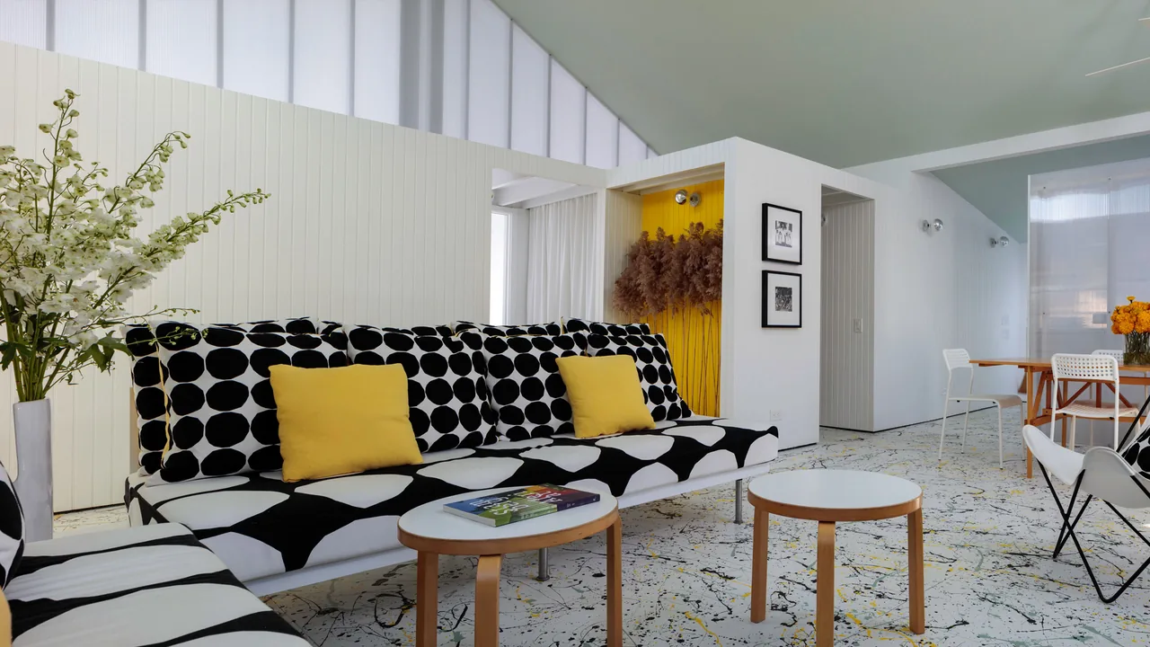 Living room with black and white patterned sofa, yellow pillows, and a yellow accent wall niche with dried plants.