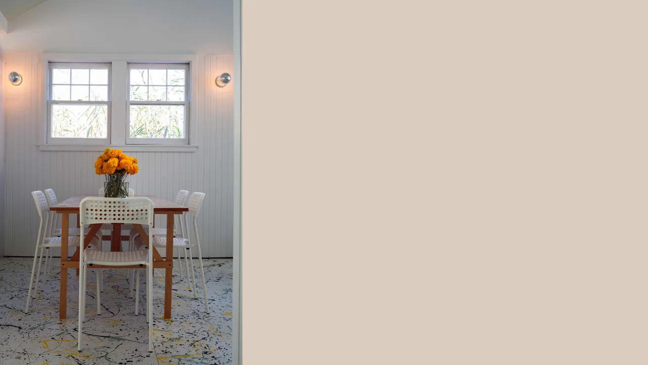 Dining area features a wooden table with white perforated chairs and a painted concrete floor, centered beneath two windows.