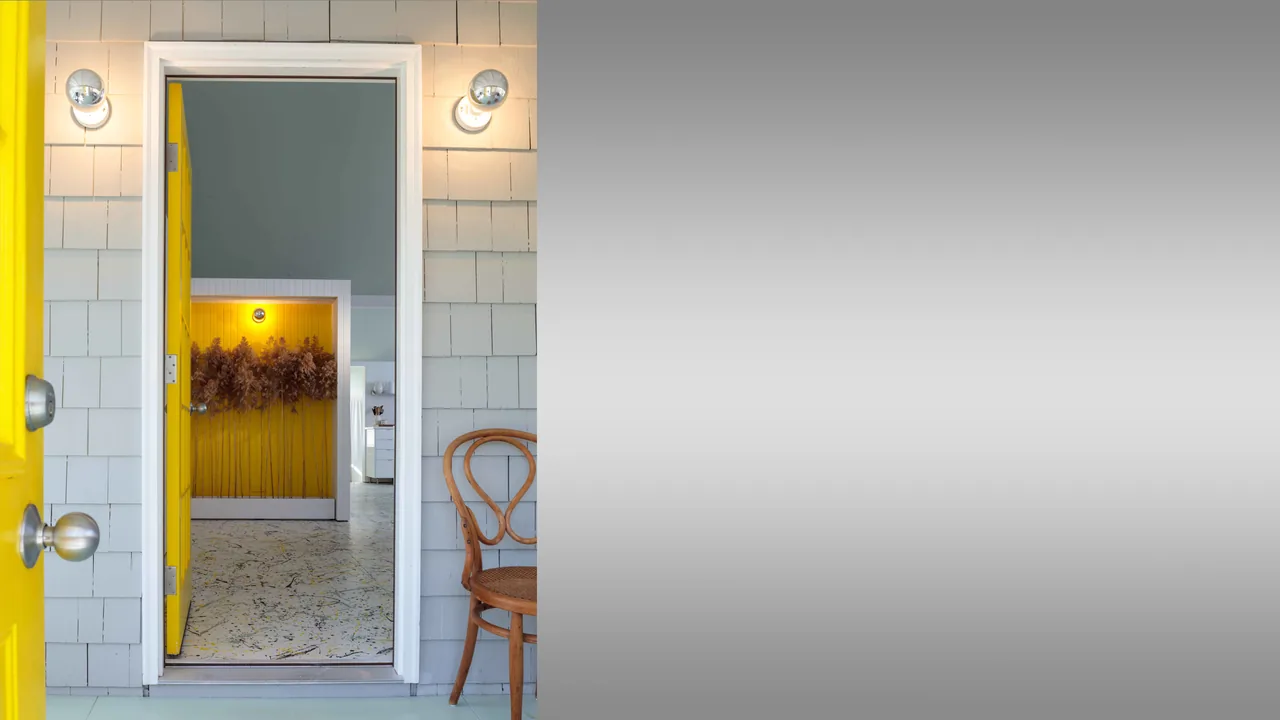 Entry door painted yellow opens into a room with yellow paneling and dried floral wall art.