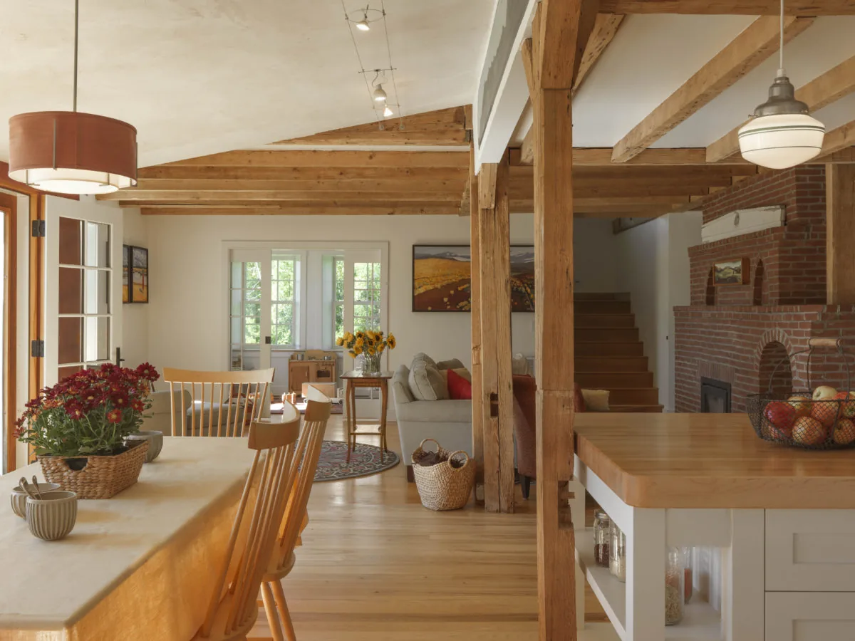 Open dining and living space featuring wooden beams, a brick arch fireplace, and a wooden countertop kitchen island.