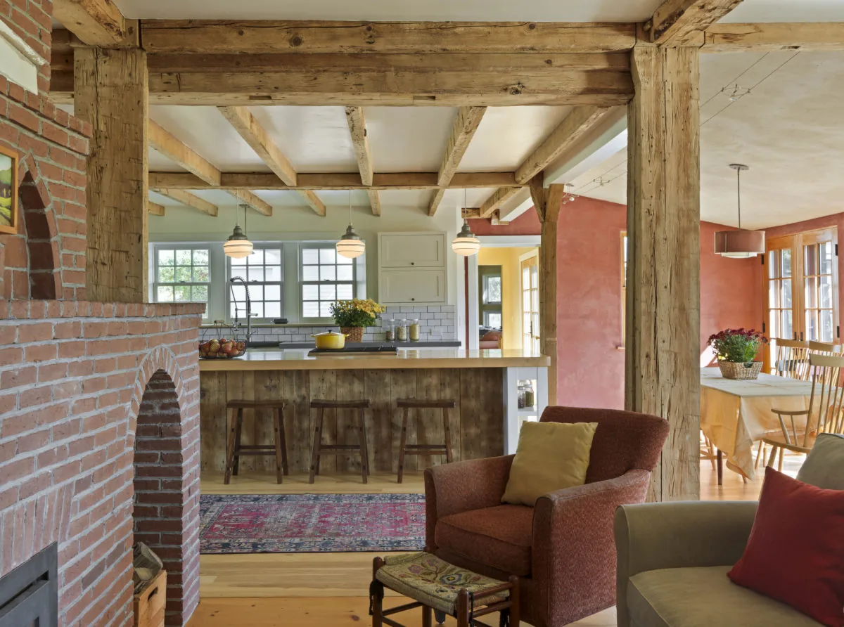 Rustic interior featuring exposed wood beams, brick fireplace, and an open kitchen with wooden island and pendant lights