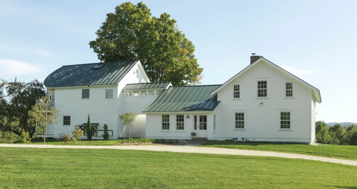 Quaker Street house by Studio III architects features white siding and green metal roofs in a rural setting.