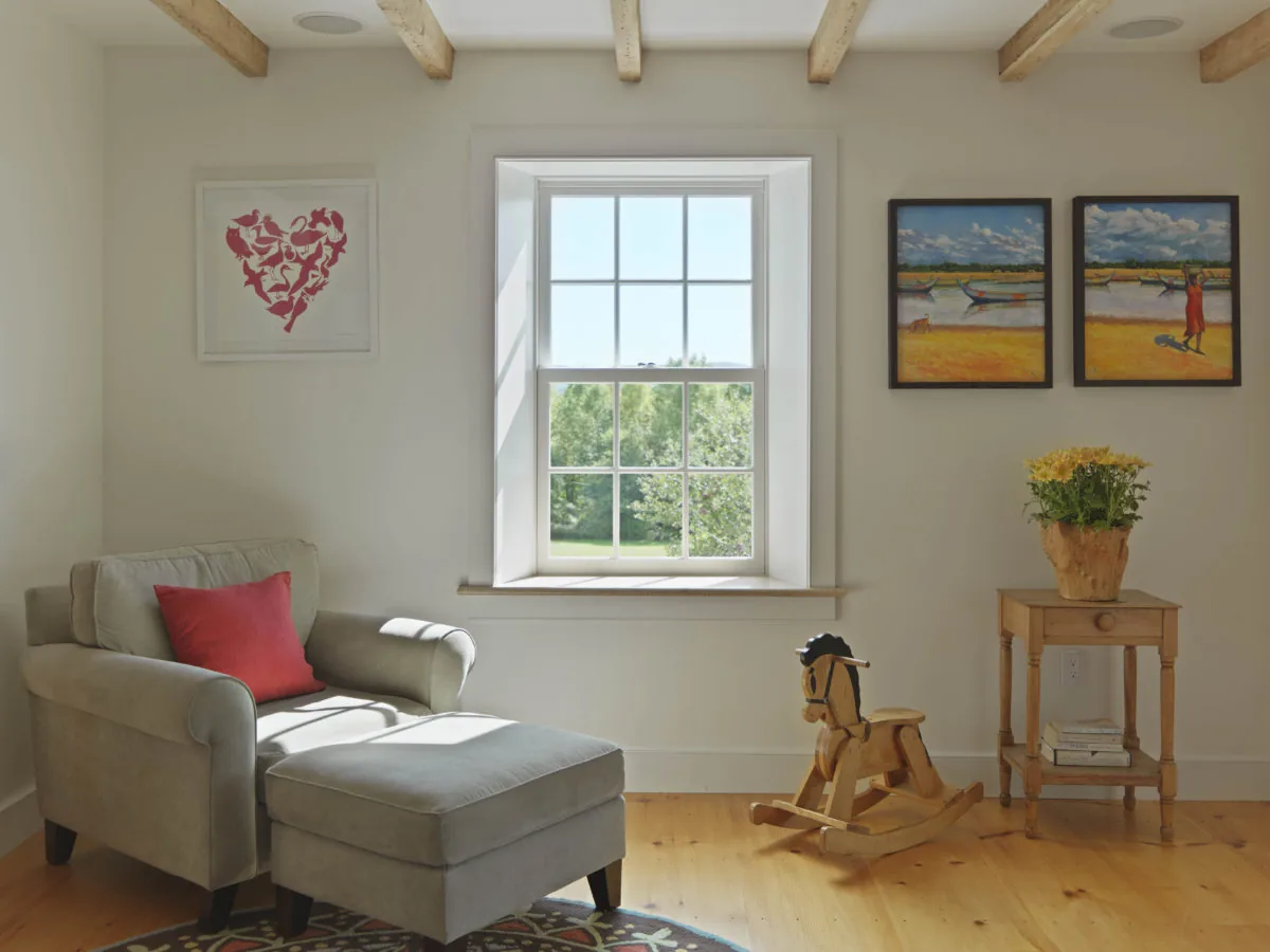 Cozy living room corner features an upholstered armchair with ottoman near a window framed with divided lites.