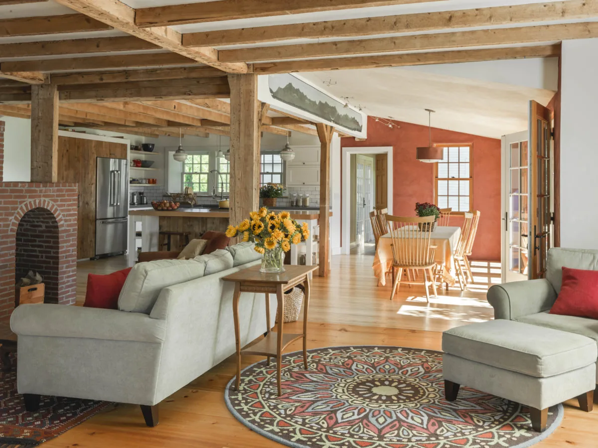 Living room and dining area with rustic wooden beams, a brick arch fireplace, and natural wood flooring at Quaker Street project.