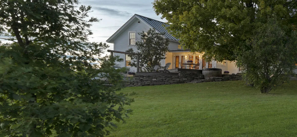 Quaker Street Hilltop House by Studio III architects in rural setting with glowing interior lights in early evening.