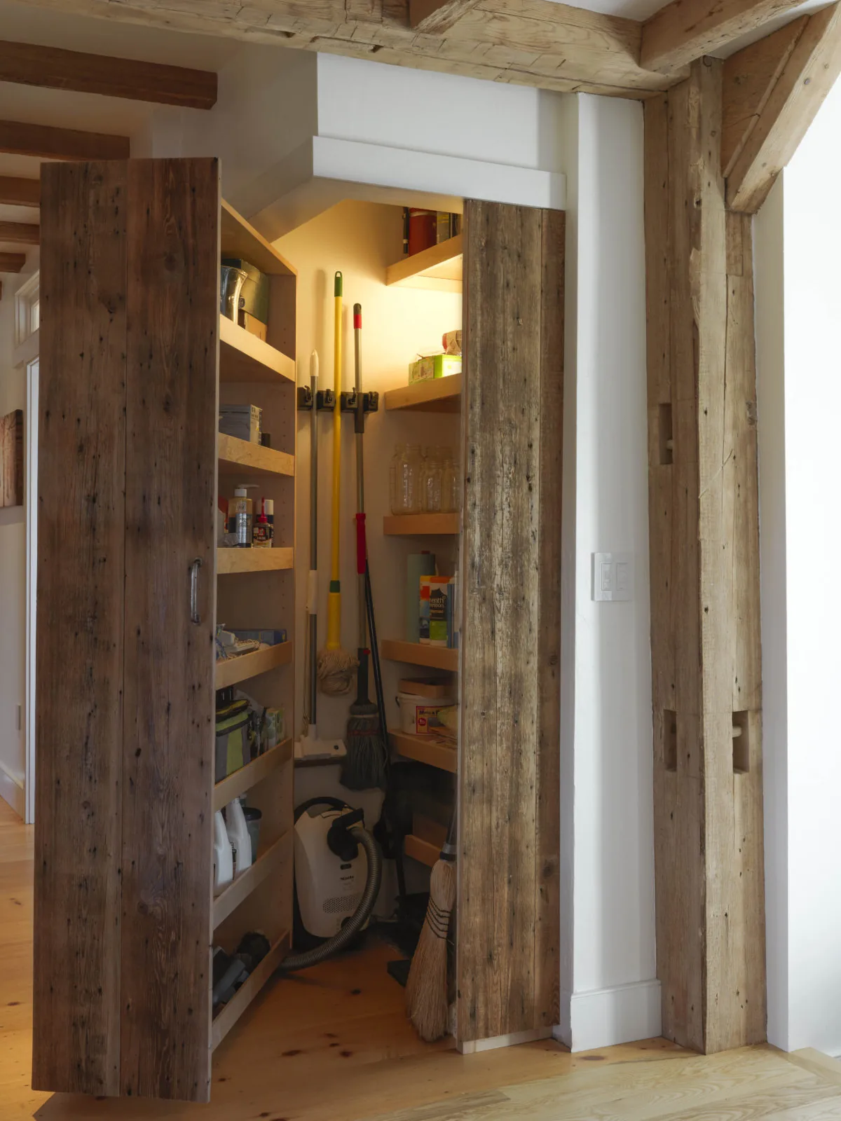 Storage pantry with rustic wooden bi-fold doors and built-in shelving containing household items and cleaning tools.