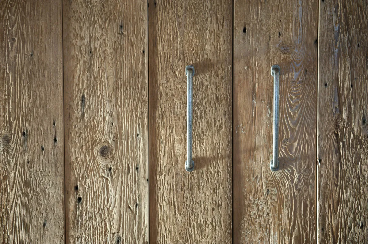 Two metal handles mounted on weathered vertical wooden planks with a textured surface.