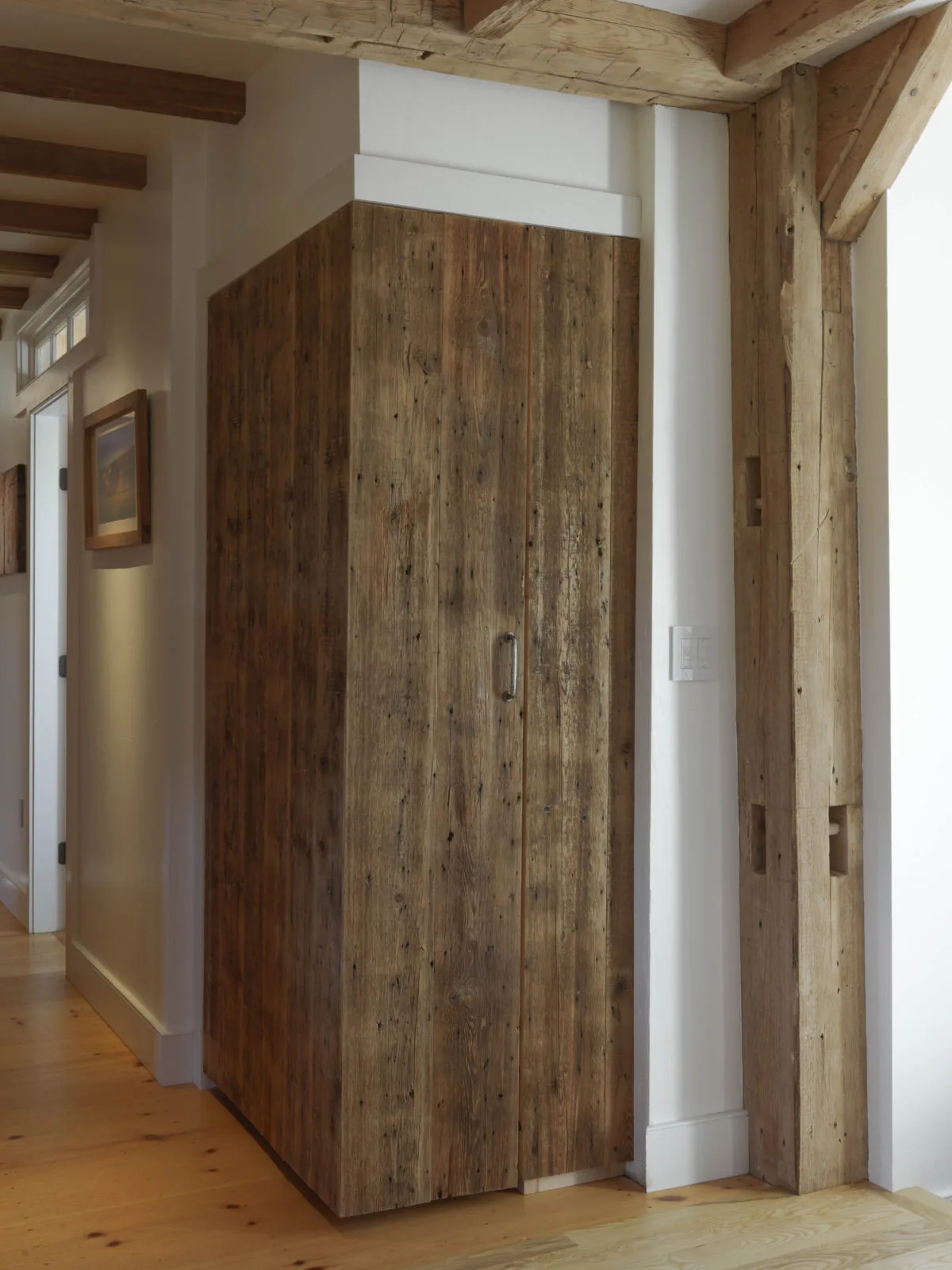 A hallway closet features rustic reclaimed wood cladding and exposed wooden ceiling beams.