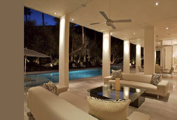 Outdoor living area with sofas and a view of a rectangular pool at night.