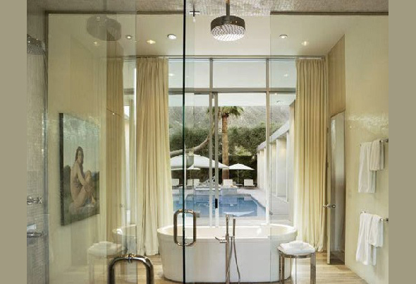 Modern bathroom featuring a freestanding tub and floor-to-ceiling glazing overlooking the pool.