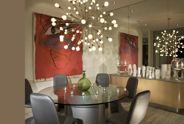 Dining area with a round glass table and gray chairs illuminated by a spherical multi-bulb pendant light, accented by bold red mural art.