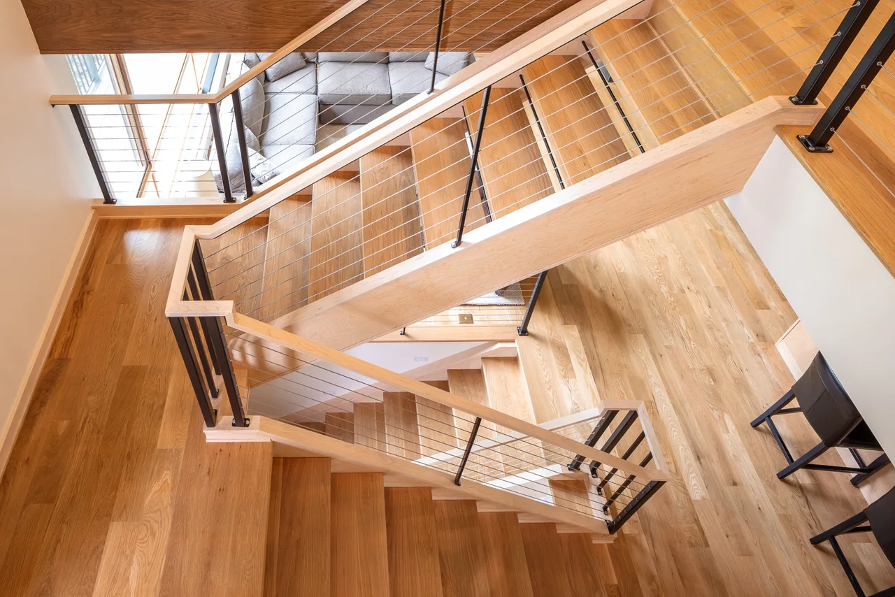 The River Residence features a wooden staircase with metal cable railings, highlighting the use of natural wood flooring.