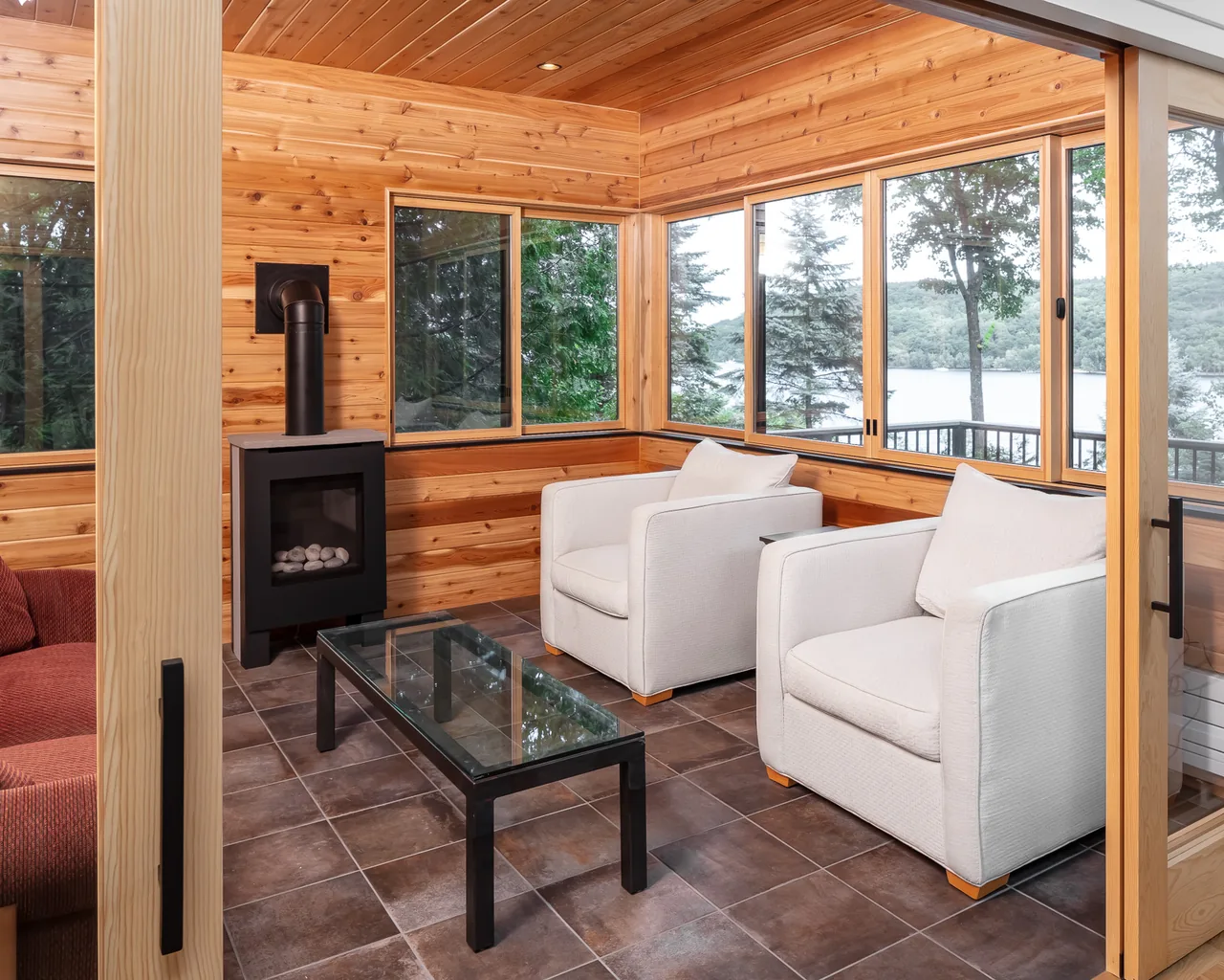 Sitting area in the River Residence features wood walls, a black stove, and floor-to-ceiling windows with a river view.