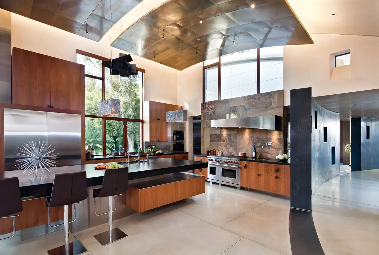 The Saratoga Creek House kitchen features wood cabinetry, black countertops, and expansive windows that bring in natural light.