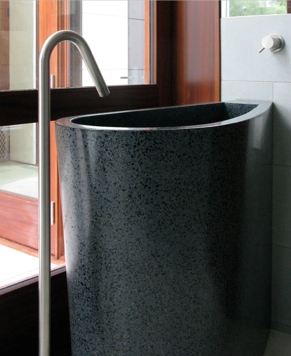 Dark stone freestanding tub with tall stainless steel faucet by a window in Saratoga Creek House bathroom.