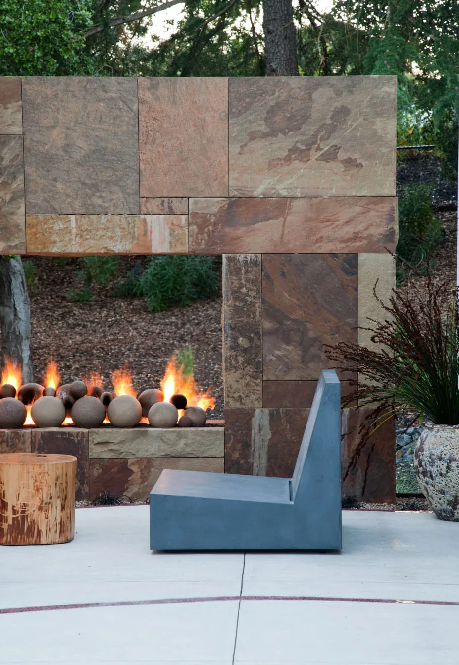 The Saratoga Creek House features an outdoor stone fireplace with spherical fire elements and modern seating.