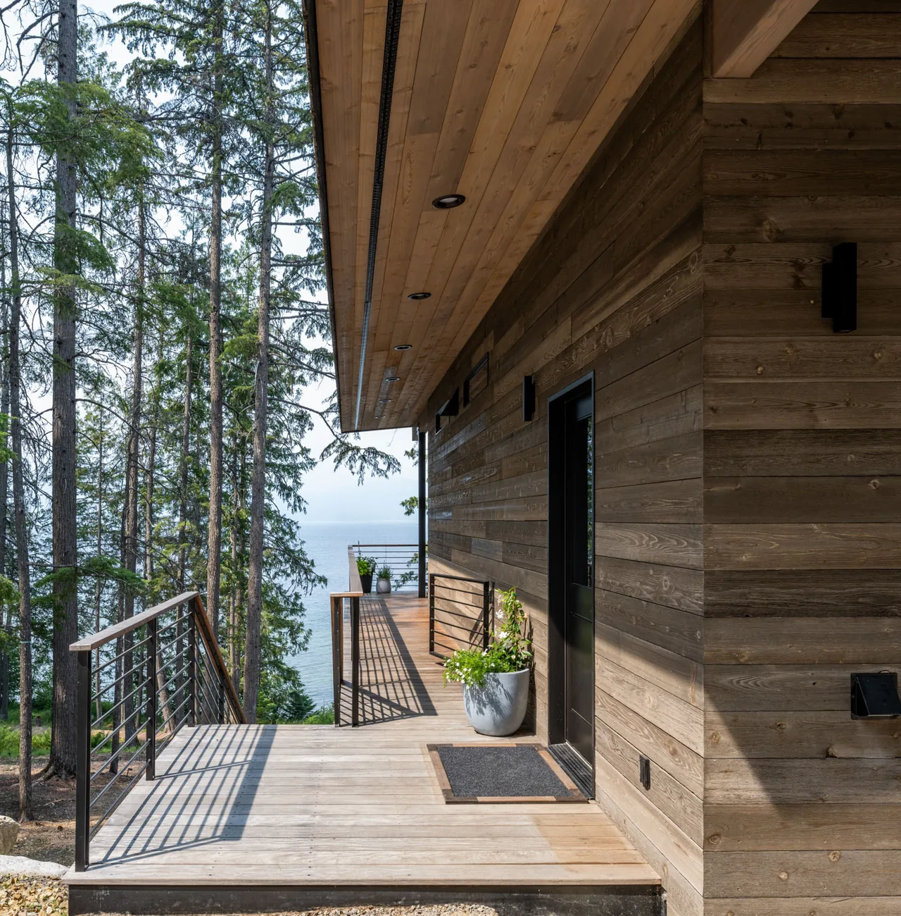 Exterior front deck of Cedars Cabin with wood siding and metal railings overlooking a lake and forest.