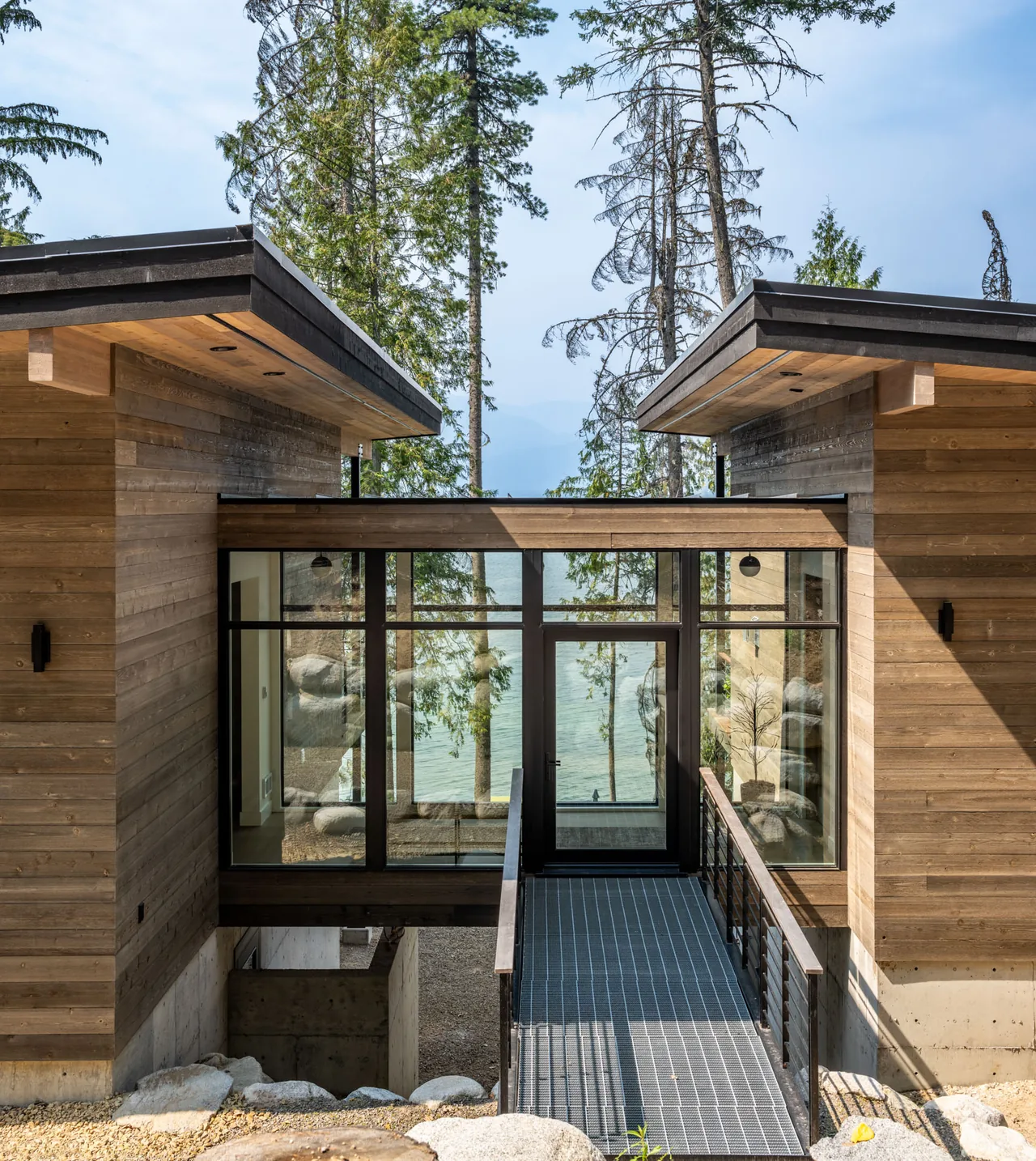 Cedars Cabin features a wood-clad exterior with a flat roof and a glass corridor joining two parts over a metal bridge.