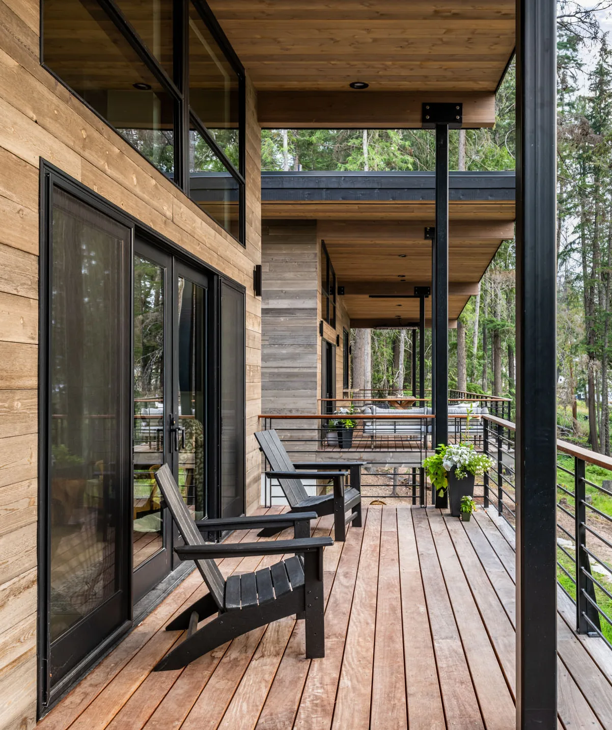 Wooden deck of Cedars Cabin features black Adirondack chairs and metal railings with a forest view.